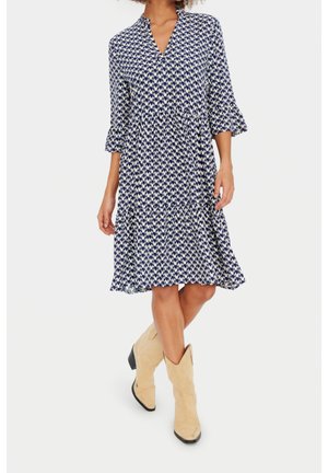 Marineblauwe en witte jurk met patroon, V-hals, driekwart mouwen en gerimpelde zoom, gecombineerd met lichtbruine cowboylaarzen.