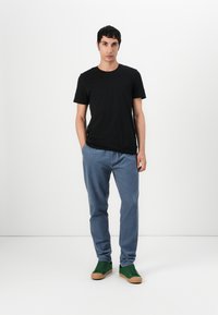 T-shirt en coton noir, pantalon bleu clair et baskets vertes avec semelles en gomme. Design simple avec une coupe confortable et sans logos visibles.