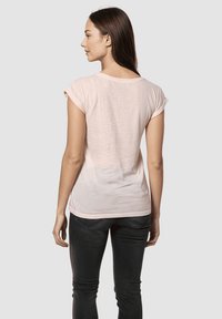 Camiseta de algodón rosa claro con mangas cortas y escote redondeado, con un diseño ajustado y textura suave, combinada con jeans oscuros.
