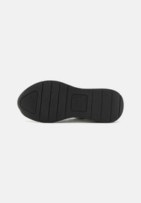 Suola di scarpe in gomma nera con grip testurizzato, caratterizzata da scanalature orizzontali e una punta arrotondata. Logo impresso nella zona del tallone.