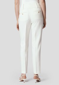 Białe, dopasowane spodnie o gładkiej teksturze, w kroju slim fit, z tylnymi kieszeniami. Złote akcenty hardware'u podkreślają projekt.
