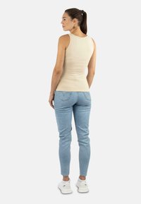 Beige Tanktop mit figurnahem Design, kombiniert mit hellblauen Skinny-Jeans und weißen Sneakers. Der Stoff wirkt glatt und dehnbar.