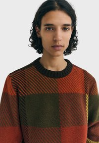 Pull en maille avec un motif de blocs multicolores dans des tons d'orange, de vert et de marron. Encolure ronde et poignets côtelés. Texture douce.