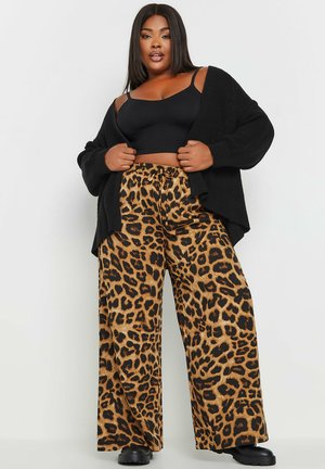 Cardigan en maille noire sur un haut noir ajusté et un pantalon large à imprimé léopard avec des accents noirs et une taille à cordon.