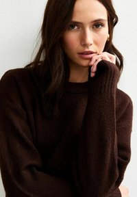 Brązowy sweter dziany z prążkowanym dekoltem i mankietami. Miękka tekstura, luźny krój i lekko oversize'owy design.