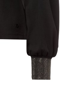 Zwarte sweatshirt met een geplooide mouw en een getextureerde manchette versierd met zilveren studs, voorzien van een klein schedel logo op het lichaam.