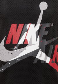 Czarna siateczkowa tkanina z dużym logo "NIKE AIR" w kolorze czerwonym, białym i szarym, z sylwetką koszykarza w akcji.