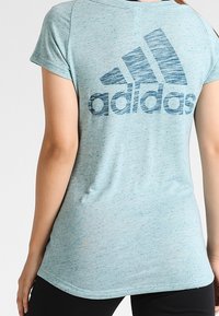 Vaaleansininen, lyhythihainen paita, joka on valmistettu pehmeästä ja teksturoidusta kankaasta. Takana on suuri tummansininen Adidas-logo.