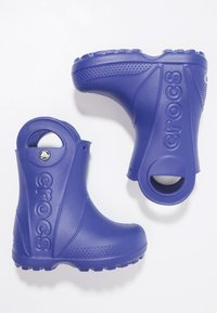 Botas de lluvia de goma moradas con lados altos, suelas con agarre texturizado, recortes circulares y logo de la marca grabado en la superficie exterior.