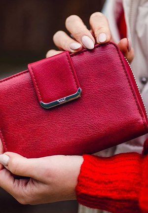 Red leather wallet with a faux leather texture, featuring a snap closure and a metallic accent. The wallet is held in a hand.