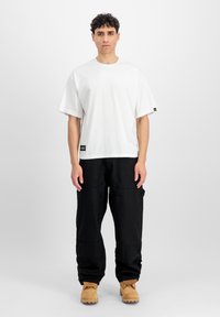 Witte katoenen t-shirt met een relaxte pasvorm, korte mouwen en een zwart logotag. Gecombineerd met zwarte cargo broeken en tan werkschoenen.