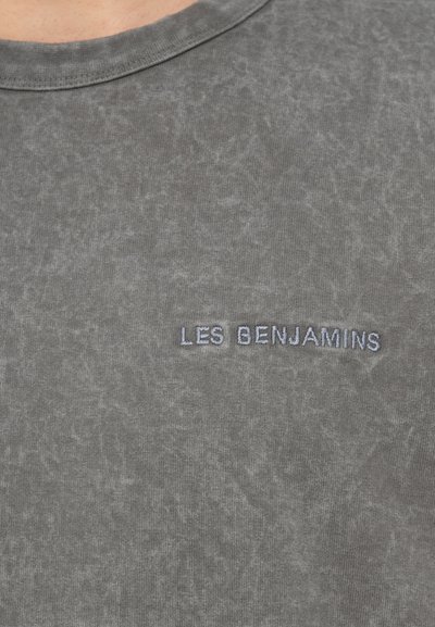Szürke pamutpóló, texturált felülettel és kerek nyakkivágással, bal oldali mellrészen kék "LES BENJAMINS" hímzéssel.