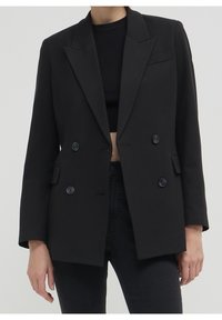 Blazer noir à double boutonnage avec grands revers, deux boutons et poches latérales. Design ajusté avec une texture lisse et une forme structurée.