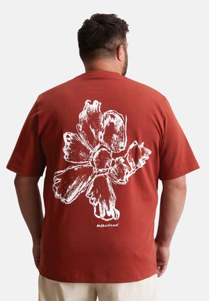 Rostfarbiges Grafik-T-Shirt mit einem großen weißen Blumendesign auf der Rückseite. Aus Baumwolle; kurze Ärmel, runder Halsausschnitt.