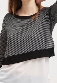 Sweat-shirt court rayé noir et blanc avec une bande noire à l'ourlet, fabriqué en tissu doux, doté d'un col rond et de manches longues.