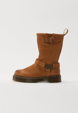 Botte en cuir marron mi-hauteur avec des sangles à boucle autour de la cheville et du haut, coutures jaunes et semelle épaisse crantée.