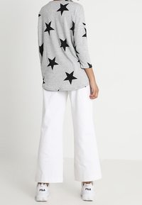 Pullover grigio con motivo a stella nera, maniche a tre quarti; abbinato a pantaloni bianchi a gamba larga e sneakers bianche.