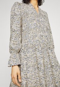 Långärmad klänning med v-ringning. Tillverkad av lättviktig tyg med ett flerfärgat abstrakt mönster i beige, blått och svart.