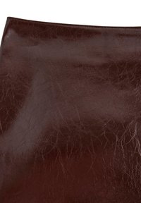 Superficie in pelle lucida marrone scuro con pieghe naturali e texture visibili, che mette in mostra l'aspetto usurato e lucido del materiale.