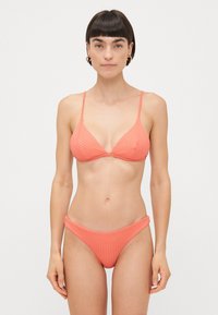 Coral ribbed bikini set featuring a triangular bralette with thin straps and matching high-waisted bottom, both made from stretchy fabric.