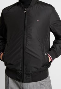 Sort bomberjakke lavet af glat nylon, med fuld lynlås, ribbede manchetter, sidelommer og et lille logo på venstre bryst.