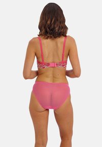 Bralette de encaje rosa con tirantes ajustables y cierre de gancho, combinado con unas braguitas semi-transparentes rosa a juego.