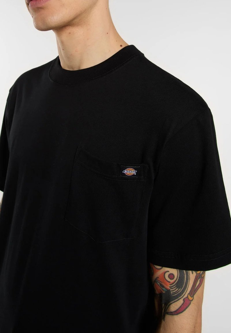 T-shirt nera a maniche corte in cotone, con una tasca sul petto e una toppa con il logo. Design semplice con scollo classico rotondo.