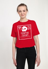 Rød bomulds t-shirt med et grafikdesign af et kranium og teksten "CENTRE COURT RACKET CLUB" i hvid. Korte ærmer, afslappet pasform.