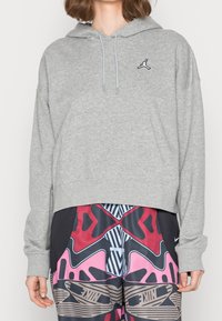 Sudadera con capucha de color gris claro, con un bolsillo canguro, dobladillo acanalado y un pequeño logo negro en el pecho. Corte holgado con mangas largas.