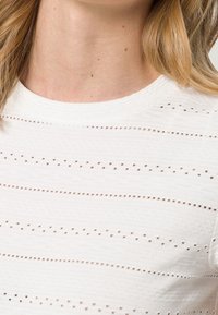 Hvid kortærmet top med tekstureret stof, med horisontale stribede udskæringer. Rund halsudskæring, glat finish og subtile mønsterdetaljer.
