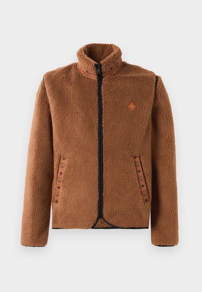 Pruun täisnööpidega fliisjakker kõrge kaelusega, tekstureeritud kangaga, musta tõmblukuga, mustriliste taskuääretega ja väikese rombikujulise rinnamärgiga.