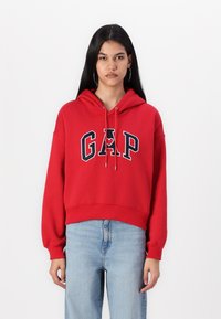 Rde skrajšani kapucar iz mehkega blaga, s velikim logotipom "GAP" v mornarsko modri barvi z belimi obrobami in prilagodljivo kapuco s vrvico.