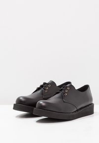 Scarpe in pelle nere con punta arrotondata, suola piatta e eyelets in tonalità oro. Texture liscia con dettagli di cucitura minimi.