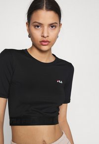T-shirt nera corta realizzata in tessuto liscio, con maniche corte e scollatura rotonda. Include un logo frontale e una banda con marchio.