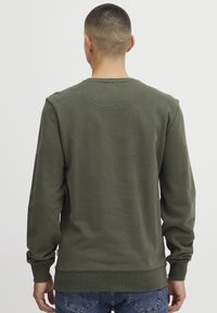 Olivenfarget genser med lange ermer, ribbestrikkede mansjetter og nederkant, myk stofftekstur og en subtil detalj på nakken bak.