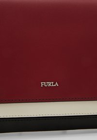 Rød, hvid og sort lædertaske sektion med sølv "FURLA" logo centreret på den røde læderpanel.