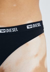 Zwarte bikinibroek met een brede elastische tailleband waarop het "DIESEL" logo in het wit staat. Glad materiaal met een aansluitende pasvorm.