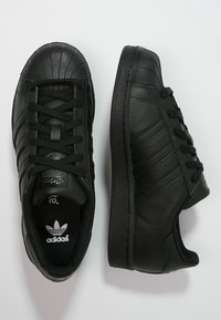 Černé kožené tenisky s texturovanou špičkou, šněrovacím designem a třemi bočními pruhy. Obsahují polstrovaný límec a logo na jazyku.