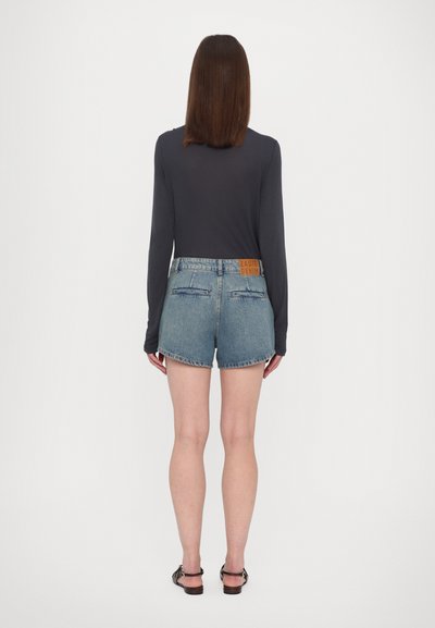 Shorts de mezclilla en un lavado azul claro con dobladillos deshilachados, bolsillos traseros y una etiqueta de cuero marrón en la cintura. Top de manga larga en color navy.