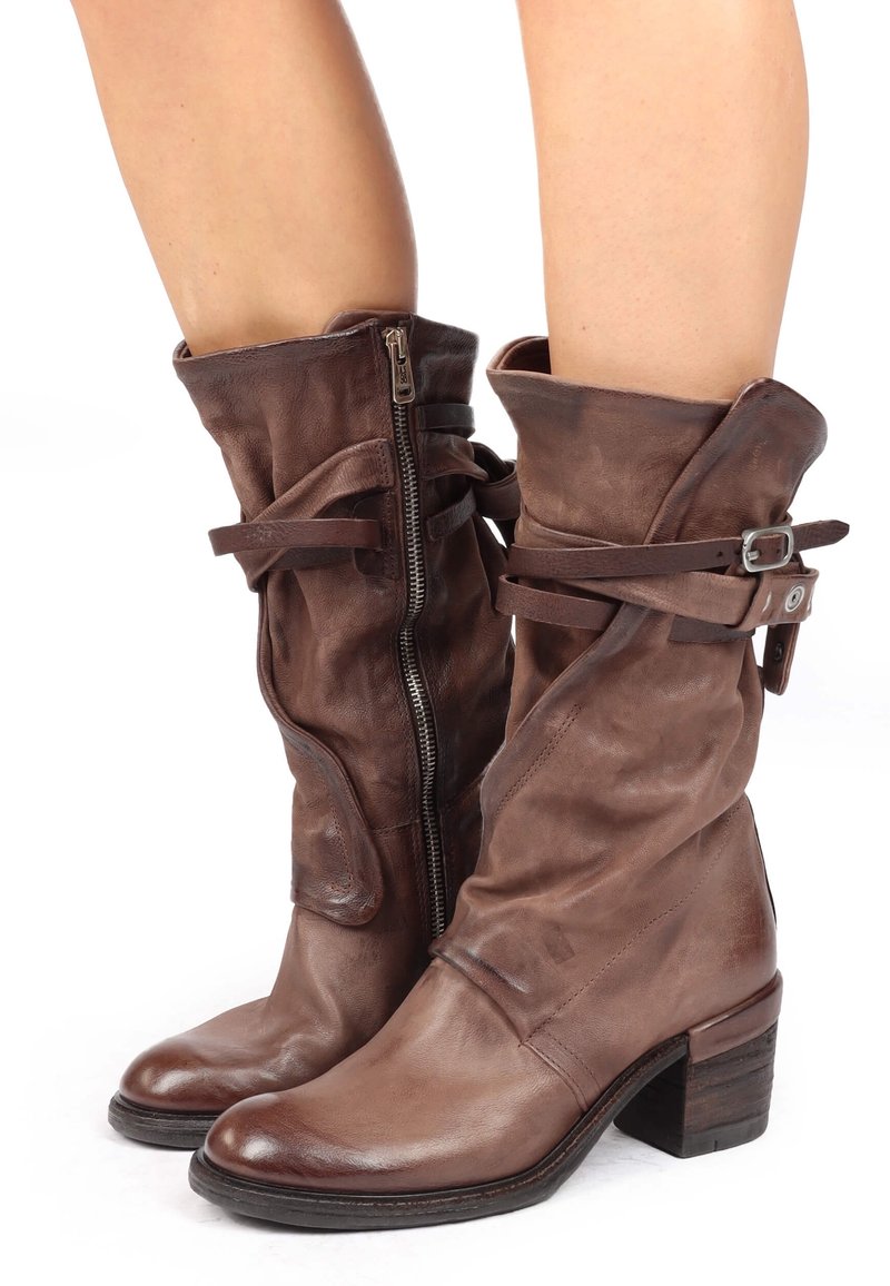Botas de cuero marrón hasta la mitad de la pantorrilla con un diseño holgado, cremallera lateral y correas ajustables, con un tacón apilado y textura suave.