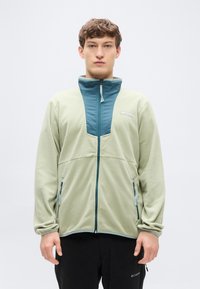 Φωτεινό πράσινο μπουφάν φλις με φερμουάρ και γιακά σε τιρκουάζ χρώμα, με φερμουάρ στο μπροστινό μέρος, πλαϊνές τσέπες και σχέδιο με μπλοκ χρωμάτων.