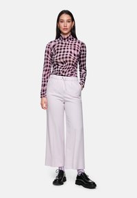 Black and pink checkered turtleneck top with long sleeves, paired with light purple wide-leg pants and black platform shoes.