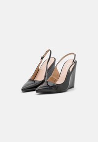 Tacchi slingback in vernice nera con zeppa, punta affusolata e cinturini alla caviglia, vista laterale inclinata su uno sfondo bianco.