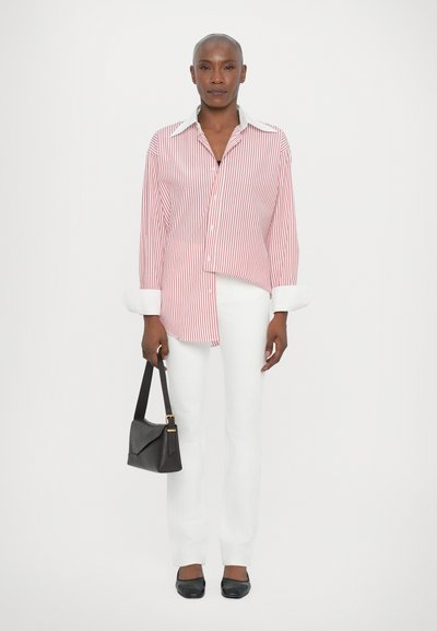 Red and white striped shirt with long sleeves and button-down collar, paired with white pants and black flats, holding a black handbag.