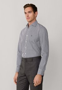 Raitapaita sinivalkoisesta kankaasta, nappikiinnitys, pitkät hihat, pieni logo rinnassa. Yhdistetty harmaisiin housuihin.