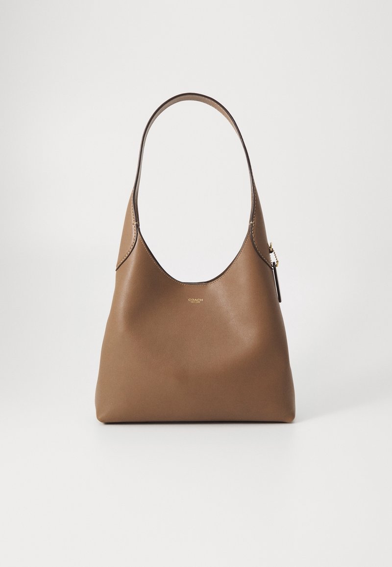 Brun läder tote-väska med en slät yta, rund form och en enkel axelrem. Har minimal hårdvara och logodetalj.