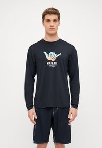 Czarna koszula z długim rękawem z grafiką przedstawiającą dłonie wykonujące znak shaka, z napisem "HAWAII" i "RIPCURL" w kontrastowych kolorach.