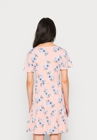 Vestido floral em tecido rosa claro com padrões de flores azuis e pretas. Mangas curtas e bainha rodada com um design de volantes em camadas.