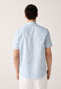 Rövid ujjú ing világoskék anyagból, fehér virágmintával. Gombos gallérral és ívelt szegéllyel rendelkezik. Simogató tapintású.