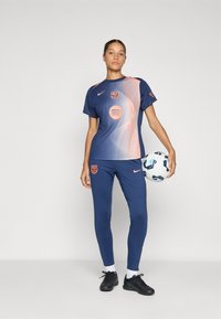Nike sportswear set in navy blue with orange accents. Features a short-sleeve shirt with logo and a textured design, paired with fitted pants.
